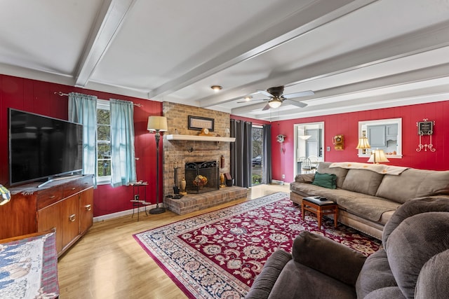 living room featuring beam ceiling, ceiling fan, light hardwood / wood-style floors, and a brick fireplace