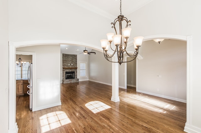 unfurnished dining area featuring crown molding, a stone fireplace, dark hardwood / wood-style flooring, high vaulted ceiling, and ceiling fan