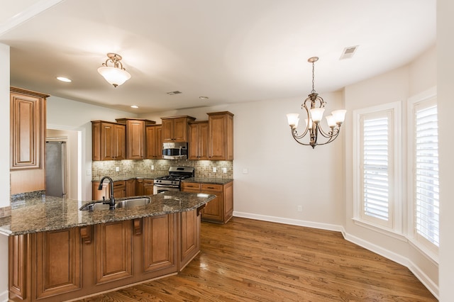 kitchen with stainless steel appliances, sink, kitchen peninsula, dark hardwood / wood-style floors, and dark stone countertops