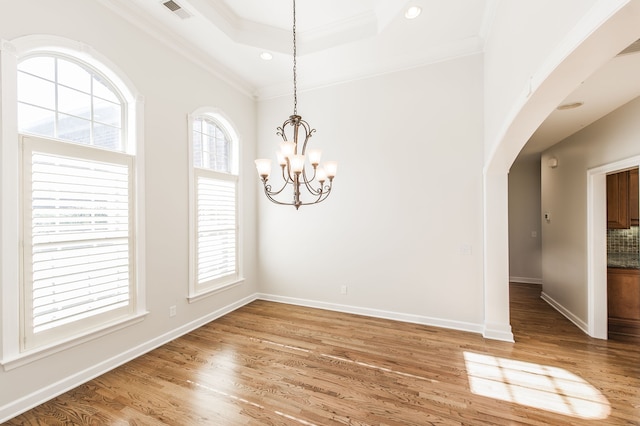 empty room with wood-type flooring, a chandelier, a raised ceiling, and ornamental molding