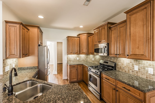 kitchen with light hardwood / wood-style floors, sink, appliances with stainless steel finishes, dark stone counters, and backsplash