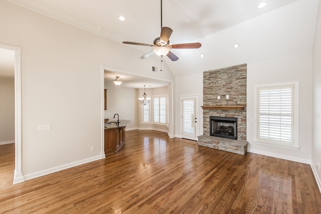 unfurnished living room featuring high vaulted ceiling, hardwood / wood-style flooring, a healthy amount of sunlight, and ceiling fan with notable chandelier