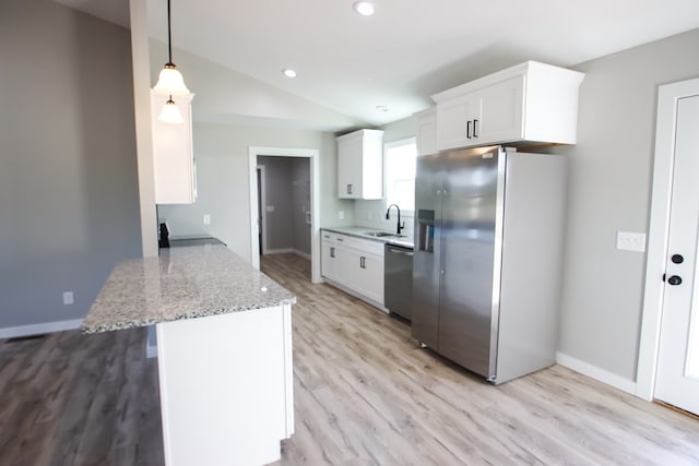 kitchen with appliances with stainless steel finishes, light stone countertops, light wood-type flooring, white cabinets, and pendant lighting