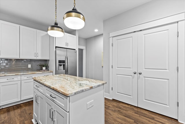 kitchen with white cabinets, hanging light fixtures, dark hardwood / wood-style floors, light stone countertops, and stainless steel fridge