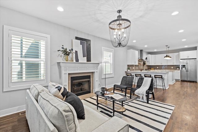 living room featuring a tiled fireplace, dark wood-type flooring, a healthy amount of sunlight, and an inviting chandelier