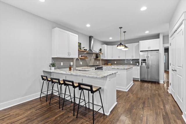 kitchen featuring stainless steel appliances, white cabinets, kitchen peninsula, wall chimney exhaust hood, and decorative light fixtures