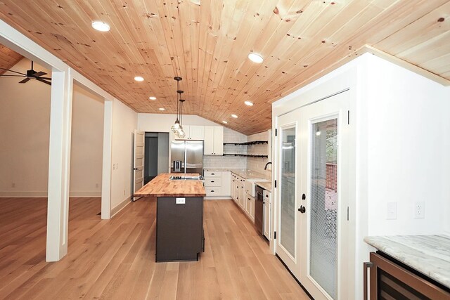 kitchen with stainless steel appliances, lofted ceiling, a center island, wood counters, and white cabinetry