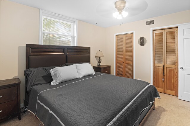 carpeted bedroom featuring ceiling fan and multiple closets