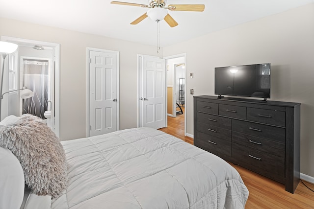 bedroom with two closets, light wood-type flooring, ensuite bathroom, and ceiling fan