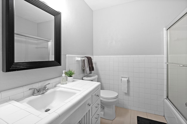 full bathroom featuring vanity, tile patterned floors, combined bath / shower with glass door, toilet, and tile walls