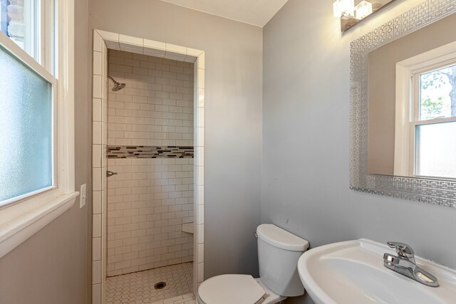 bathroom featuring toilet, a tile shower, and sink