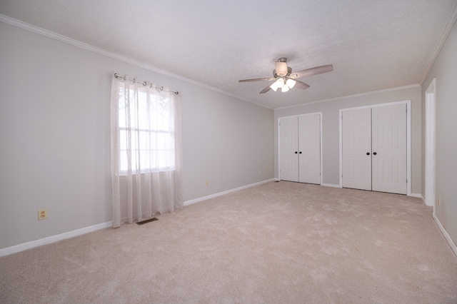 unfurnished bedroom featuring multiple closets, light carpet, ceiling fan, and crown molding