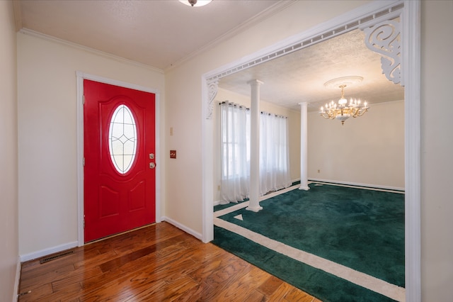 foyer with ornamental molding, dark hardwood / wood-style floors, a chandelier, and ornate columns