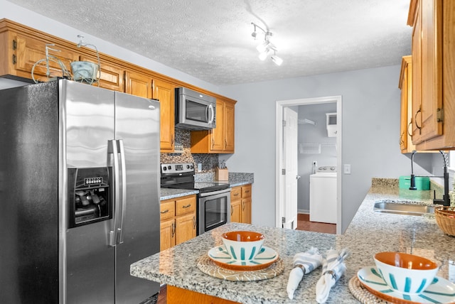 kitchen with appliances with stainless steel finishes, tasteful backsplash, light stone countertops, a textured ceiling, and washer / clothes dryer