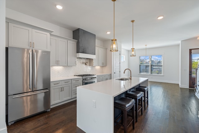 kitchen with appliances with stainless steel finishes, custom range hood, sink, decorative light fixtures, and a center island with sink