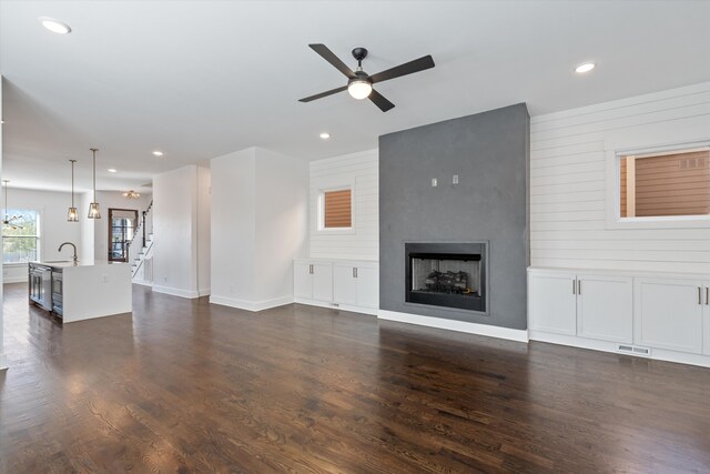 unfurnished living room with a large fireplace, ceiling fan, sink, dark hardwood / wood-style floors, and wood walls