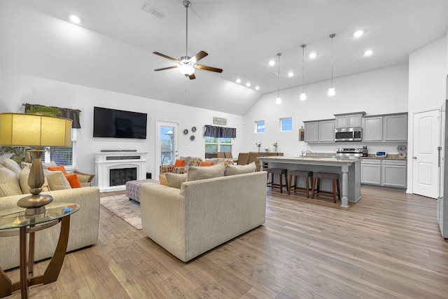 living room featuring light hardwood / wood-style floors, ceiling fan, and high vaulted ceiling