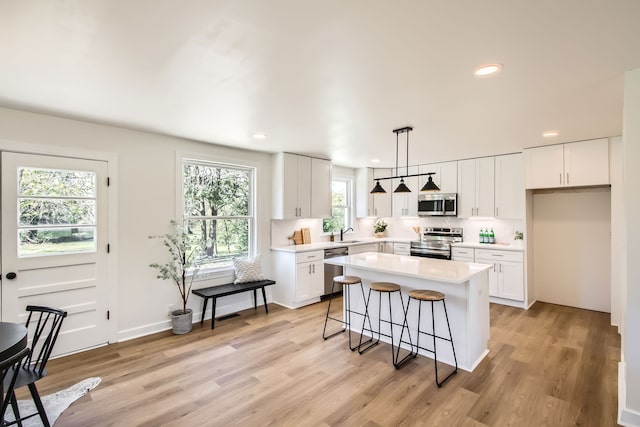 kitchen featuring light hardwood / wood-style floors, white cabinetry, appliances with stainless steel finishes, hanging light fixtures, and a center island