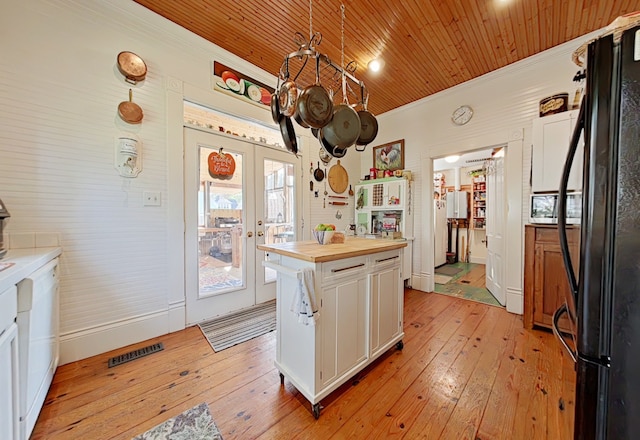 kitchen featuring wooden counters, white cabinets, black refrigerator, light hardwood / wood-style flooring, and decorative light fixtures