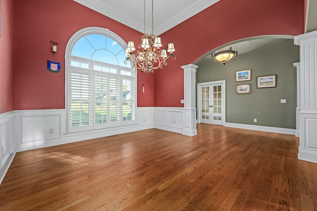 unfurnished dining area with french doors, ornate columns, a chandelier, ornamental molding, and hardwood / wood-style flooring