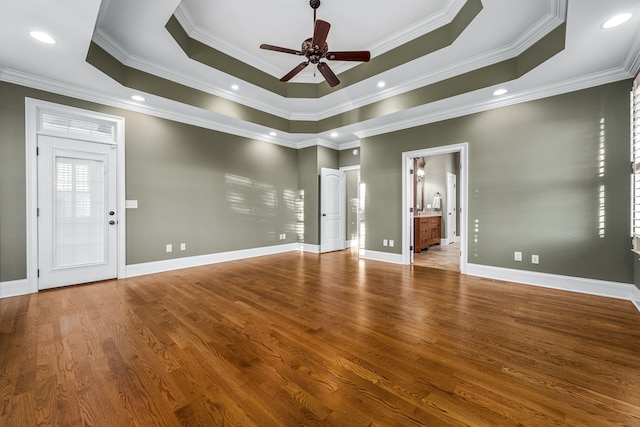 unfurnished living room featuring a raised ceiling, crown molding, hardwood / wood-style floors, and ceiling fan