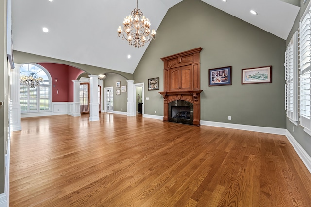 unfurnished living room featuring decorative columns, a chandelier, high vaulted ceiling, and light hardwood / wood-style flooring