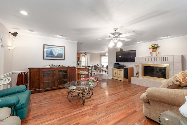 living room with light hardwood / wood-style floors, ceiling fan, crown molding, and a tile fireplace