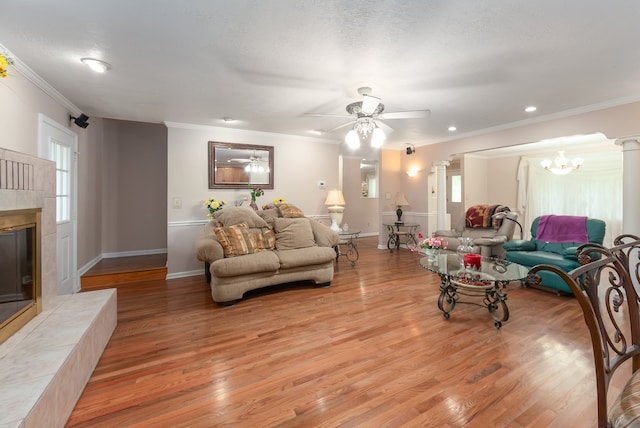 living room featuring ornamental molding, a fireplace, ornate columns, light hardwood / wood-style flooring, and ceiling fan with notable chandelier