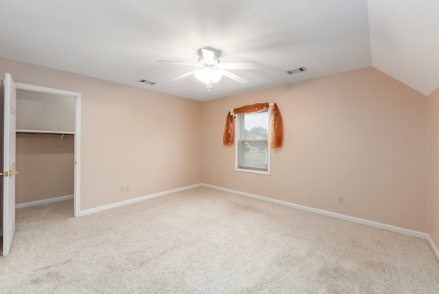 unfurnished bedroom with vaulted ceiling, light carpet, ceiling fan, a closet, and a walk in closet