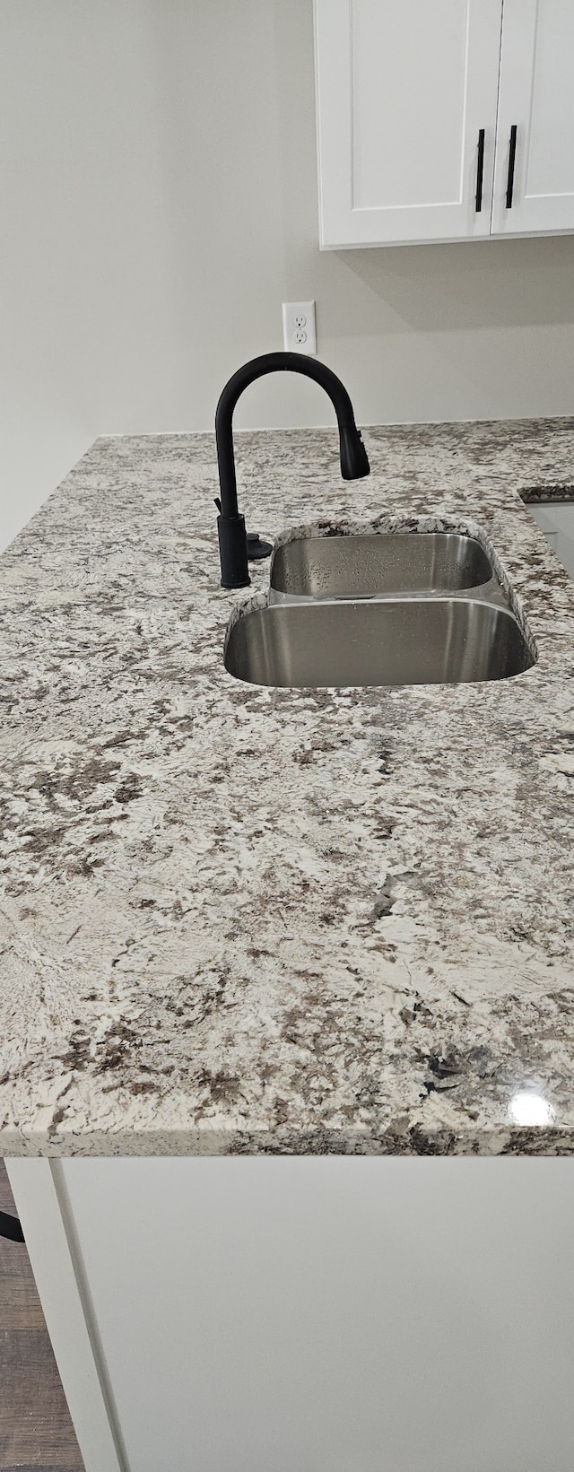 details with light stone counters, white cabinetry, and sink