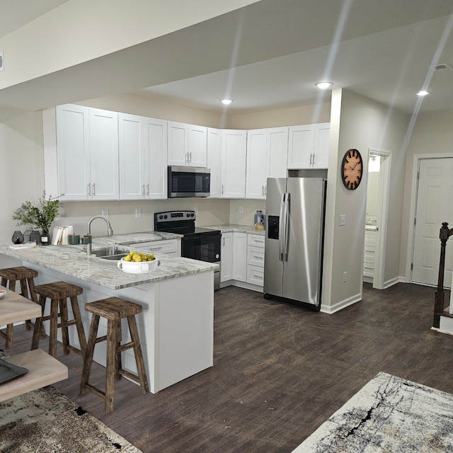 kitchen featuring a kitchen bar, kitchen peninsula, stainless steel appliances, dark wood-type flooring, and white cabinets