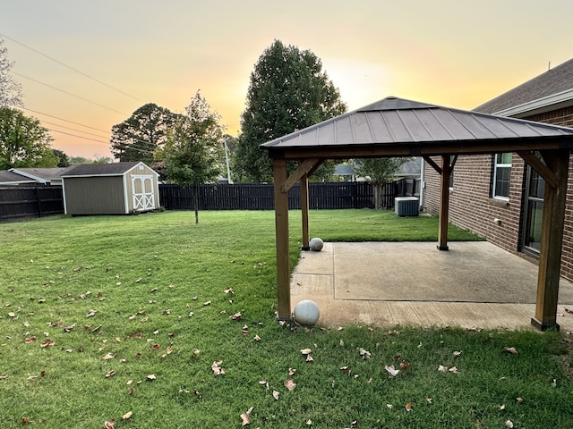 yard at dusk with a patio, a fenced backyard, an outbuilding, a gazebo, and a shed