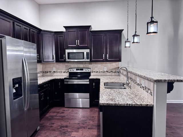 kitchen with light stone counters, pendant lighting, stainless steel appliances, tasteful backsplash, and a sink