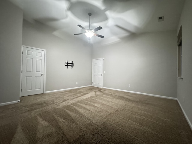 spare room featuring a ceiling fan, a high ceiling, dark carpet, and baseboards