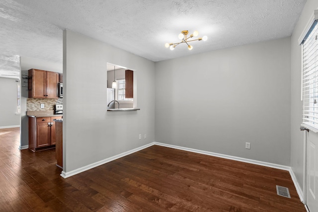 empty room with dark wood-type flooring, plenty of natural light, an inviting chandelier, and a textured ceiling