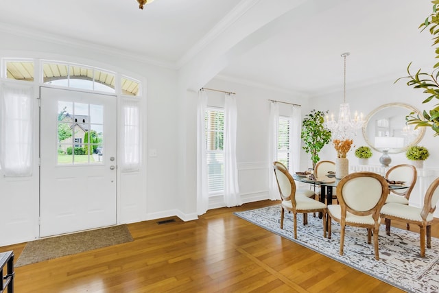 entryway featuring a wealth of natural light, wood-type flooring, an inviting chandelier, and crown molding