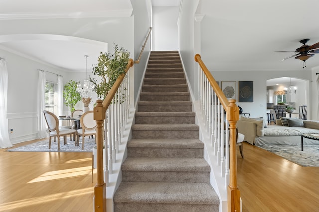 stairs featuring ornamental molding, ceiling fan with notable chandelier, and wood-type flooring