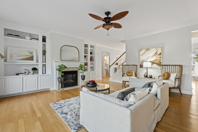 living room with a fireplace, light hardwood / wood-style floors, ceiling fan, and built in features