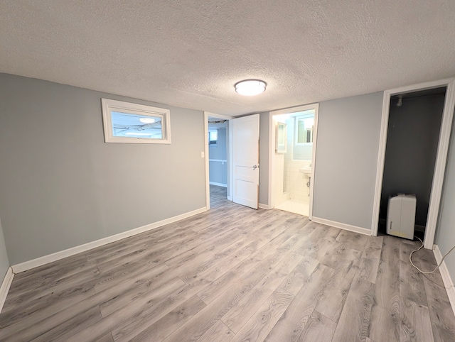 unfurnished bedroom with ensuite bathroom, light hardwood / wood-style floors, and a textured ceiling