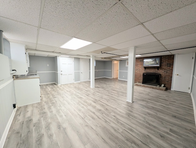 basement featuring light hardwood / wood-style flooring, a brick fireplace, and a drop ceiling