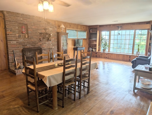 dining space with a fireplace, wood walls, hardwood / wood-style floors, and ceiling fan