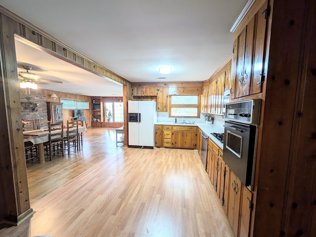 kitchen featuring ceiling fan, sink, wooden walls, black appliances, and light wood-type flooring