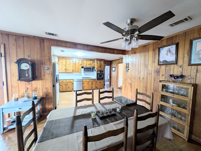 dining room featuring wooden walls, light hardwood / wood-style flooring, and ceiling fan