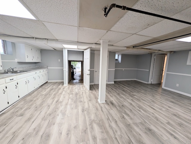 basement with a paneled ceiling, light hardwood / wood-style flooring, and sink