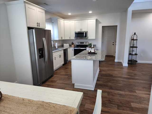 kitchen with white cabinets, stainless steel appliances, light stone countertops, and dark wood-type flooring