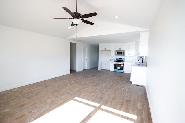 unfurnished living room featuring ceiling fan, sink, wood-type flooring, and lofted ceiling