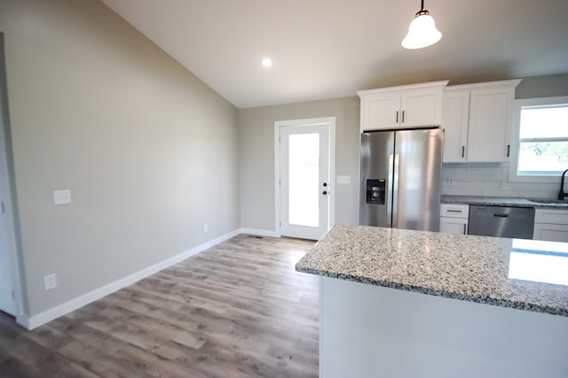 kitchen with light stone countertops, appliances with stainless steel finishes, light hardwood / wood-style floors, white cabinetry, and lofted ceiling