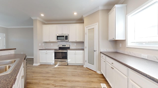 kitchen featuring white cabinetry, tasteful backsplash, crown molding, light wood-type flooring, and stainless steel appliances