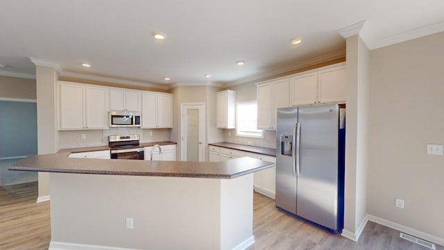 kitchen with white cabinetry, light hardwood / wood-style flooring, appliances with stainless steel finishes, a kitchen island, and ornamental molding