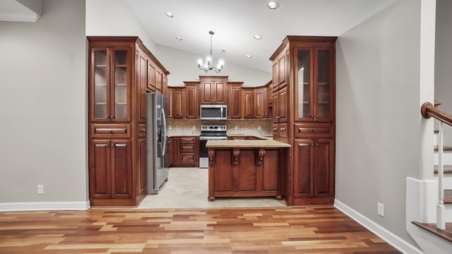 kitchen with hanging light fixtures, an inviting chandelier, vaulted ceiling, appliances with stainless steel finishes, and light wood-type flooring